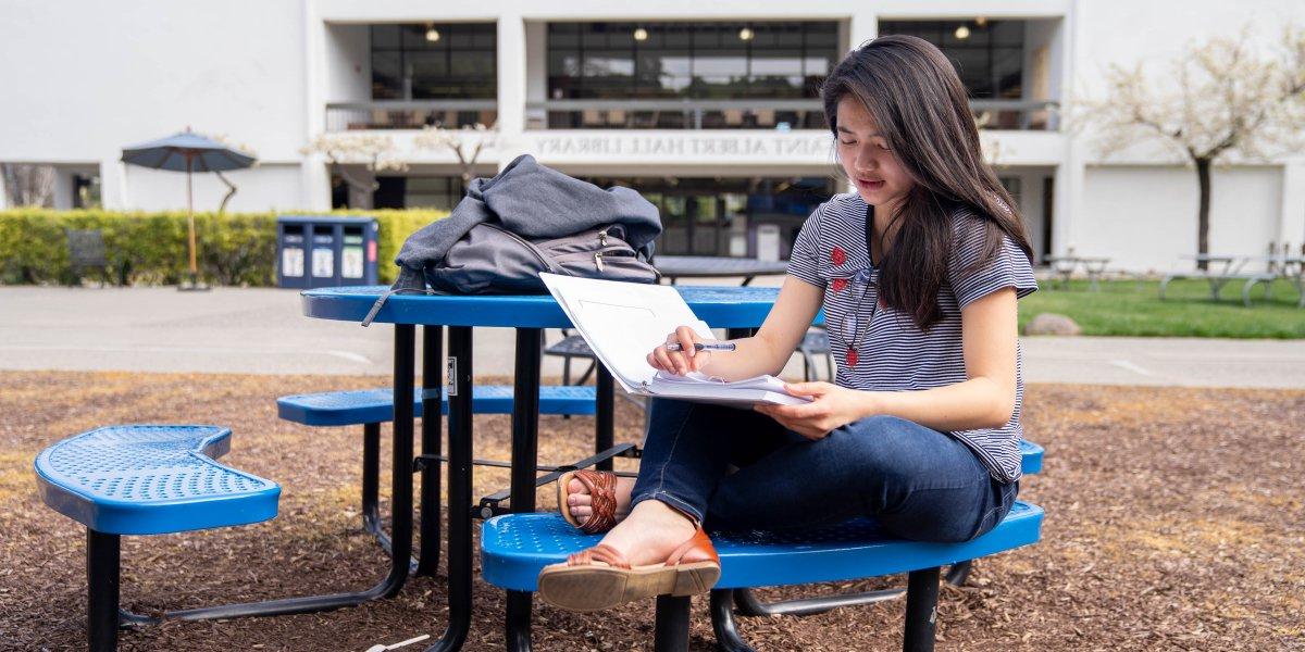 A student studying on a bench in the middle of SMC's campus